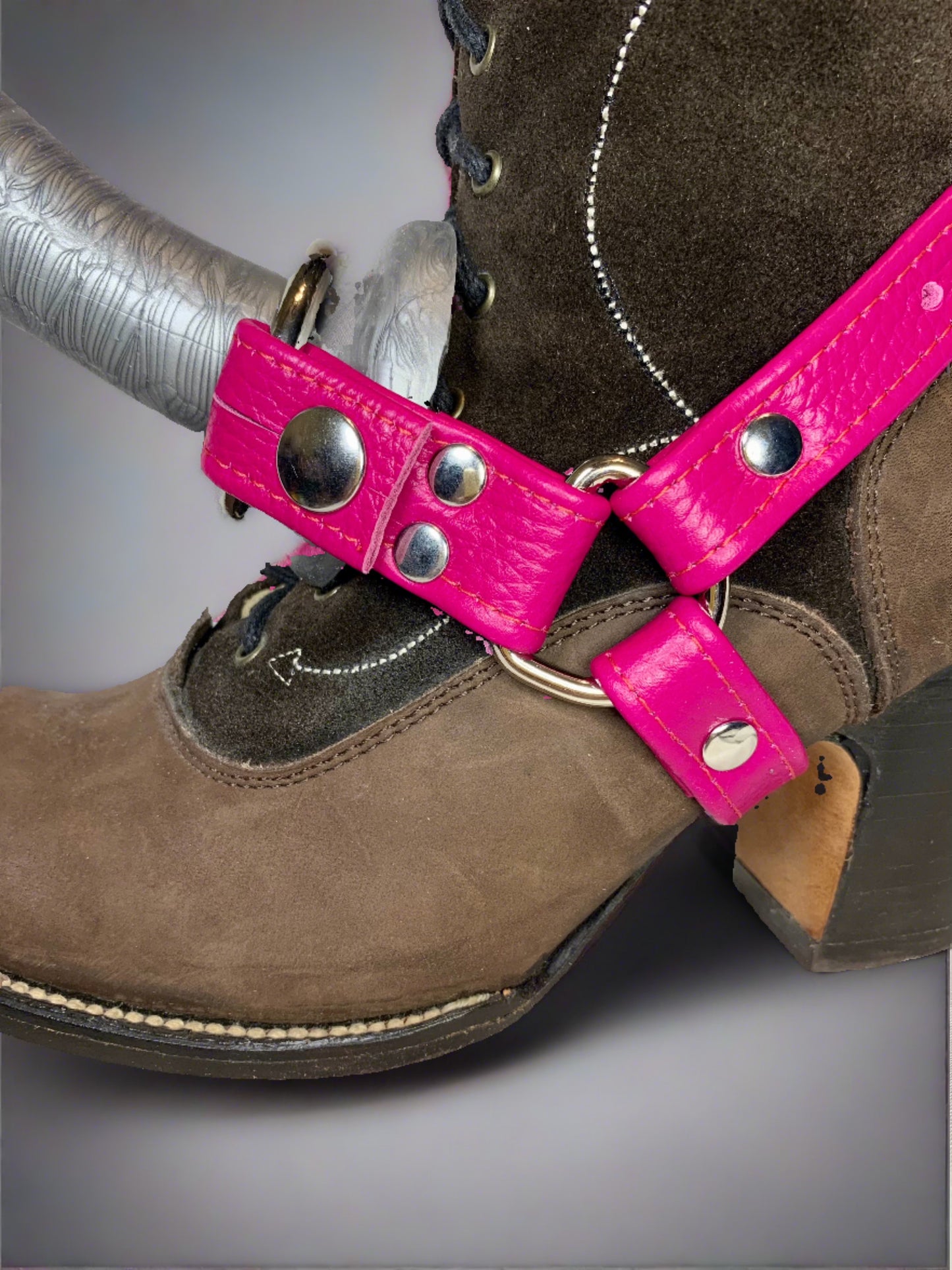 close up of brown suede boot with a magenta leather boot strapon and a silver dildo